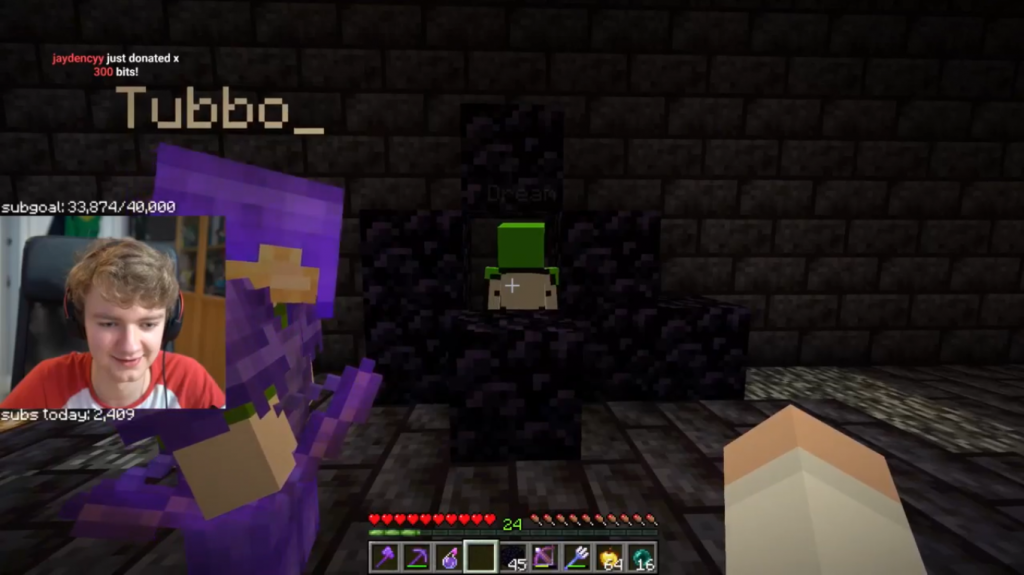 A screenshot from Tommy's stream. In front of him stands Dream in an obsidian box. Tubbo stands to his left decked out in netherite armor. Tommy's facecam shows him content and maybe gleeful.